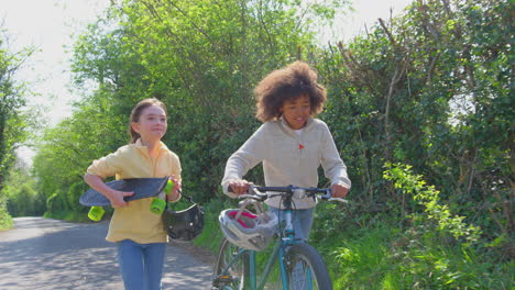 Boy-With-Bike-And-Girl-With-Skateboard-Walking-Along-Country-Road-Together