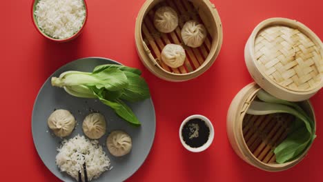 composition of plate and bamboo steamers with dim sum dumplings, pak choi and rice on red background