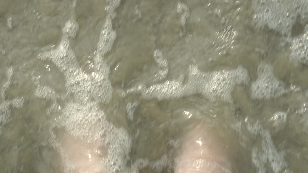 olas corriendo sobre los pies en sandalias flip flop en la playa de arena en cámara lenta