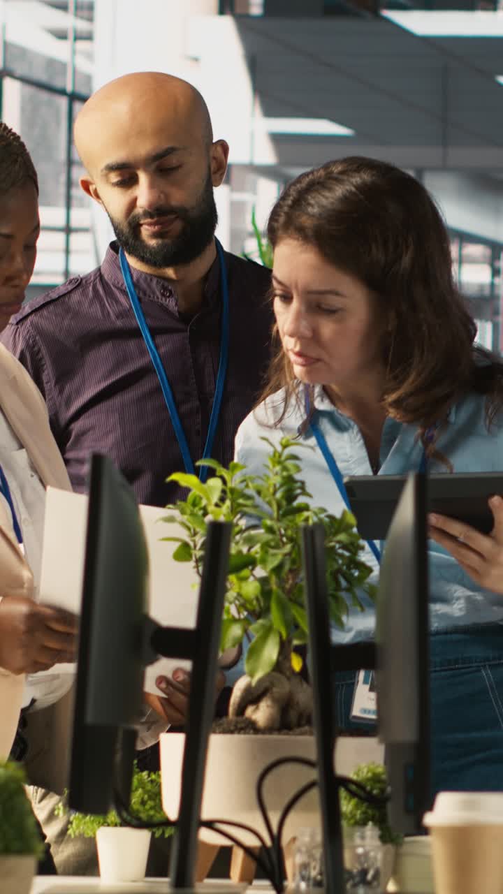 Vertical video Multiethnic coworkers looking over revenue figures on tablet in diverse office
