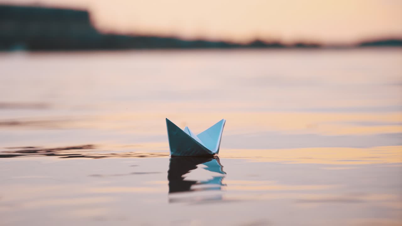 Nice paper boat on evening water surface. One blue origami ship sailing in the river calmly with its reflection outdoors.