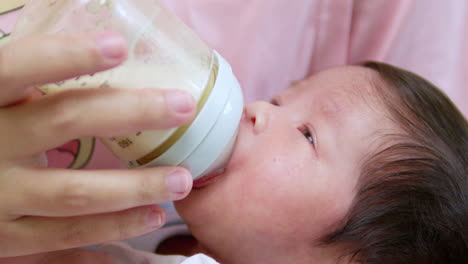 sucking some milk from a bottle as it is being fed by its mother, a newborn baby is getting some nourishment as it slowly falls asleep