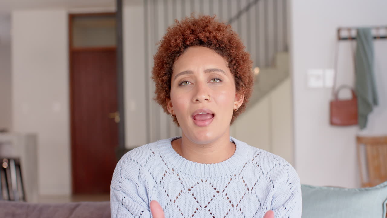 Smiling woman with curly hair gesturing while talking in cozy home setting, video call