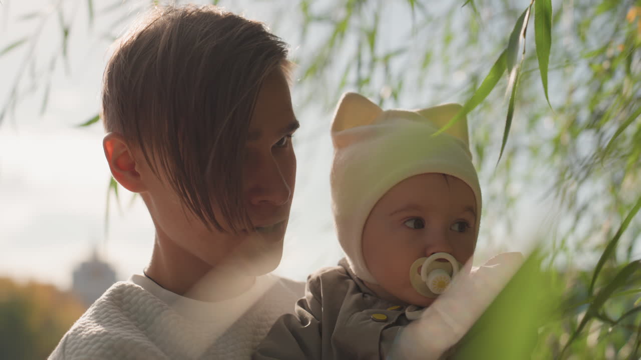 Hvid far engagerer babyen i naturen, udforsker blade og blødt lys med legende bevægelser og tæt interaktion, intimt parkportræt, der viser forbindelse, undren og moderne familiekærlighed.