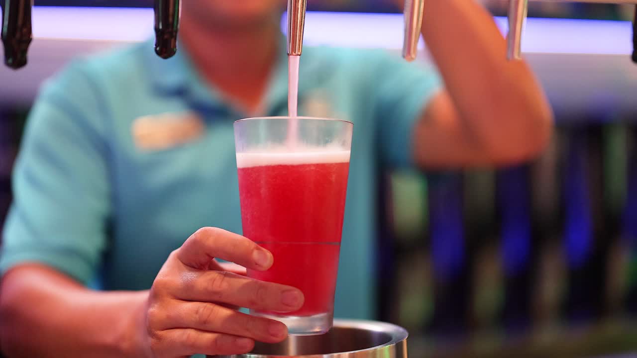 el camarero vierte una bebida roja en el vaso.