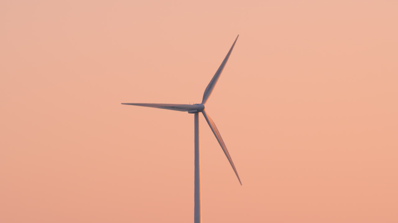 Single wind turbine turning slowly in evening light with pastel sky and minimal background, side angle telephoto isolated overview