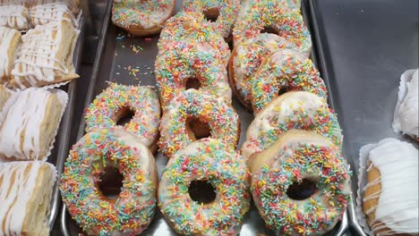 donuts with colored sprinkles being displayed at a brazilian bakery showcase.