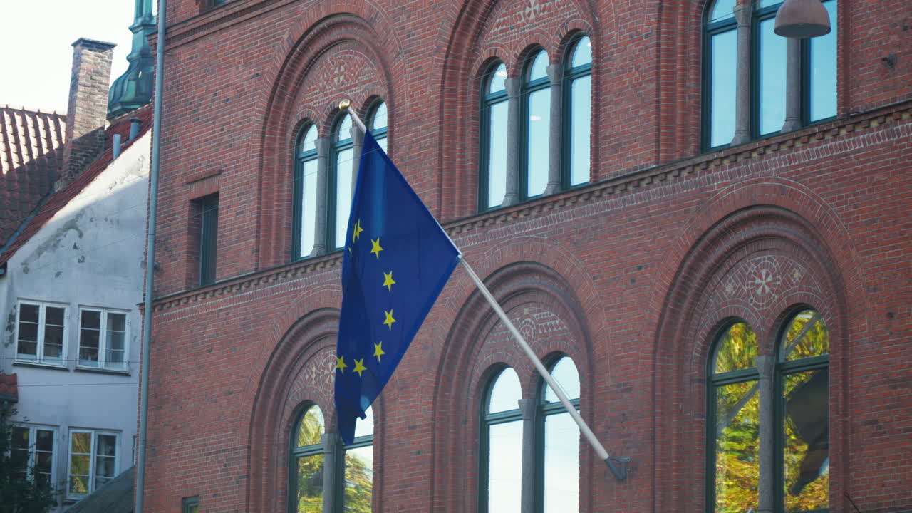 European Union flag waving outside a historic red brick building. Ideal for travel documentaries and European culture features.
