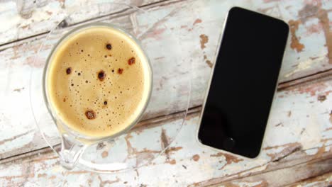 taza de café y teléfono móvil en una tabla de madera