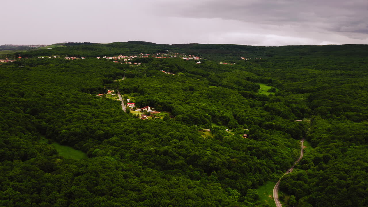 vista aérea del paisaje de drones de una carretera y un pueblo rodeado por un bosque rumano, en un día ventoso