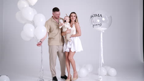 happy smiling blonde woman holding a baby and kissing her husband. beautiful caucasian family celebration with balloons.