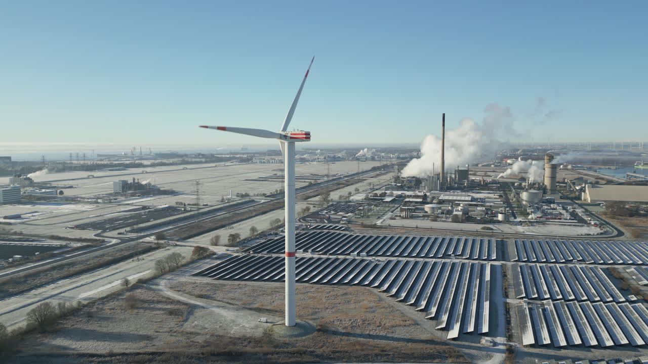 Vindmølle drejer i frostklart landskab, rygende industrianlæg, solpaneler, langsomt bagudgående, luftdroneoptagelse