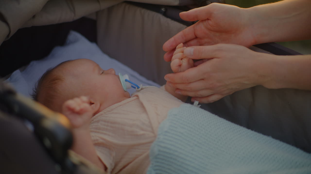 Young Mother Touching Baby's Hand in Stroller