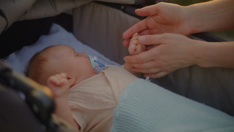young mother touching baby's hand in stroller