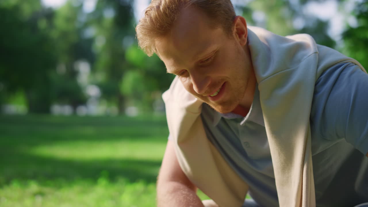 Closeup smiling handsome man sitting in squats petting animal in summer park.
