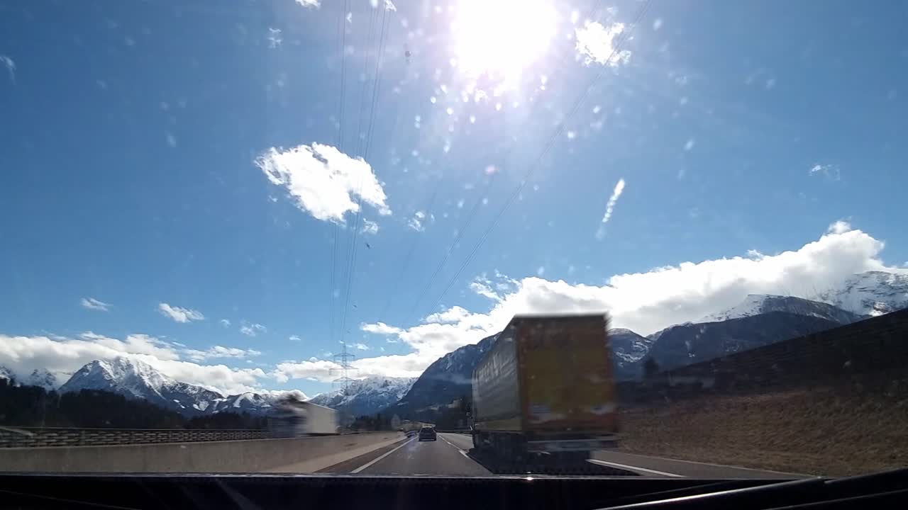 Driving Timelapse on a highway passing other cars driving on a sunny day with clear blue sky, grassy fields with trees and snow covered mountains in the distance