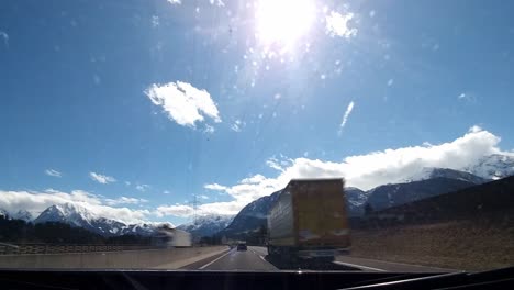 driving timelapse on a highway passing other cars driving on a sunny day with clear blue sky, grassy fields with trees and snow covered mountains in the distance