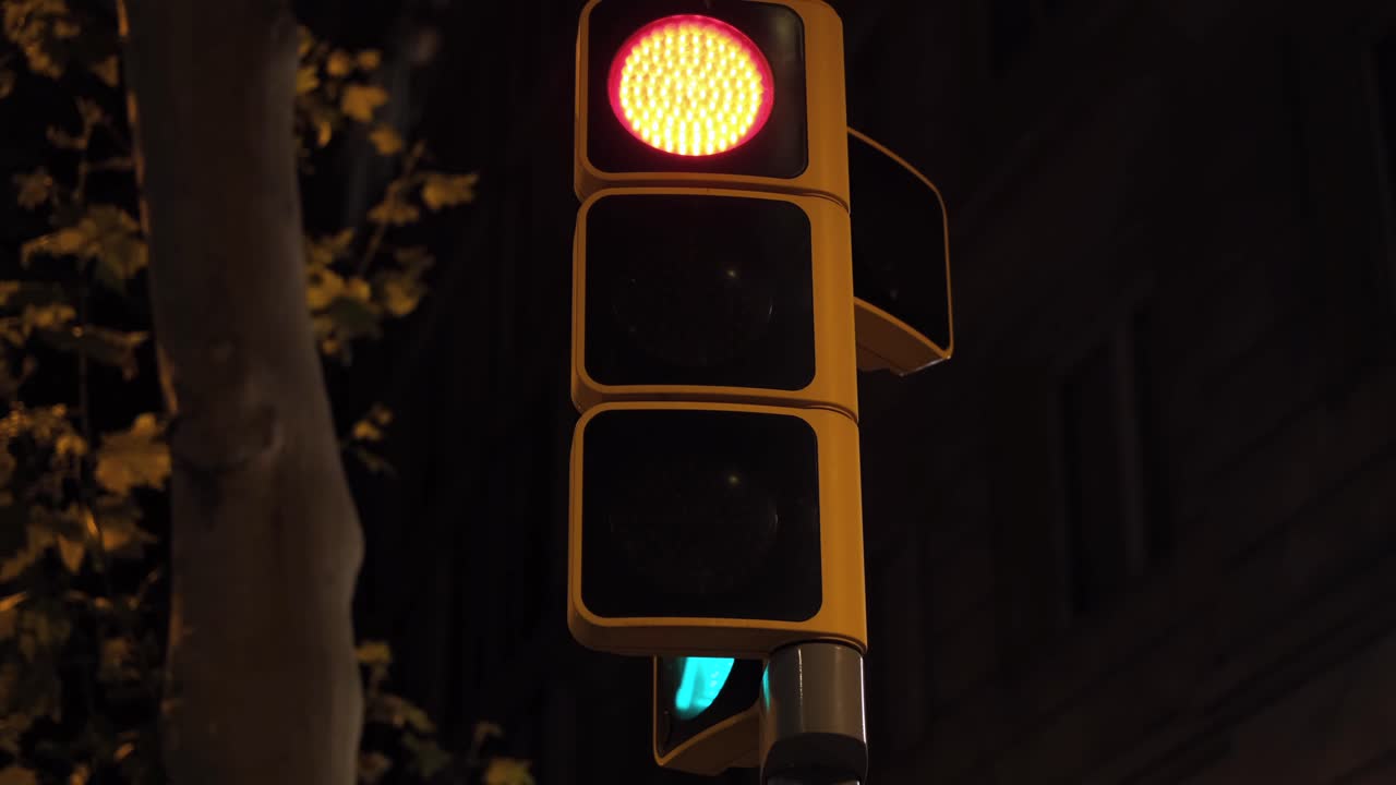 Close-up of a traffic light at night with the yellow light flashing while red and green lights remain steady. Shot in 4K with dark urban background and warm tones