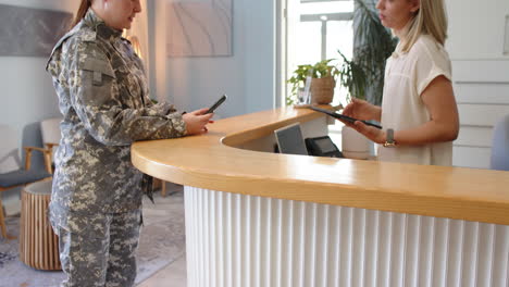 Middle-aged Caucasian woman in military uniform at reception desk with smartphone