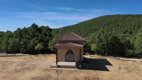 flight with close-up of a hermitage and when moving away you see that it is in a meadow with a pond surrounded by a road in a forest with the valley in the background in avila, spain