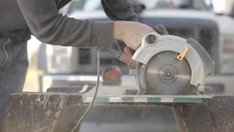 Side-view-of-hand-pushing-electric-circular-saw-cutting-through-wood-plank