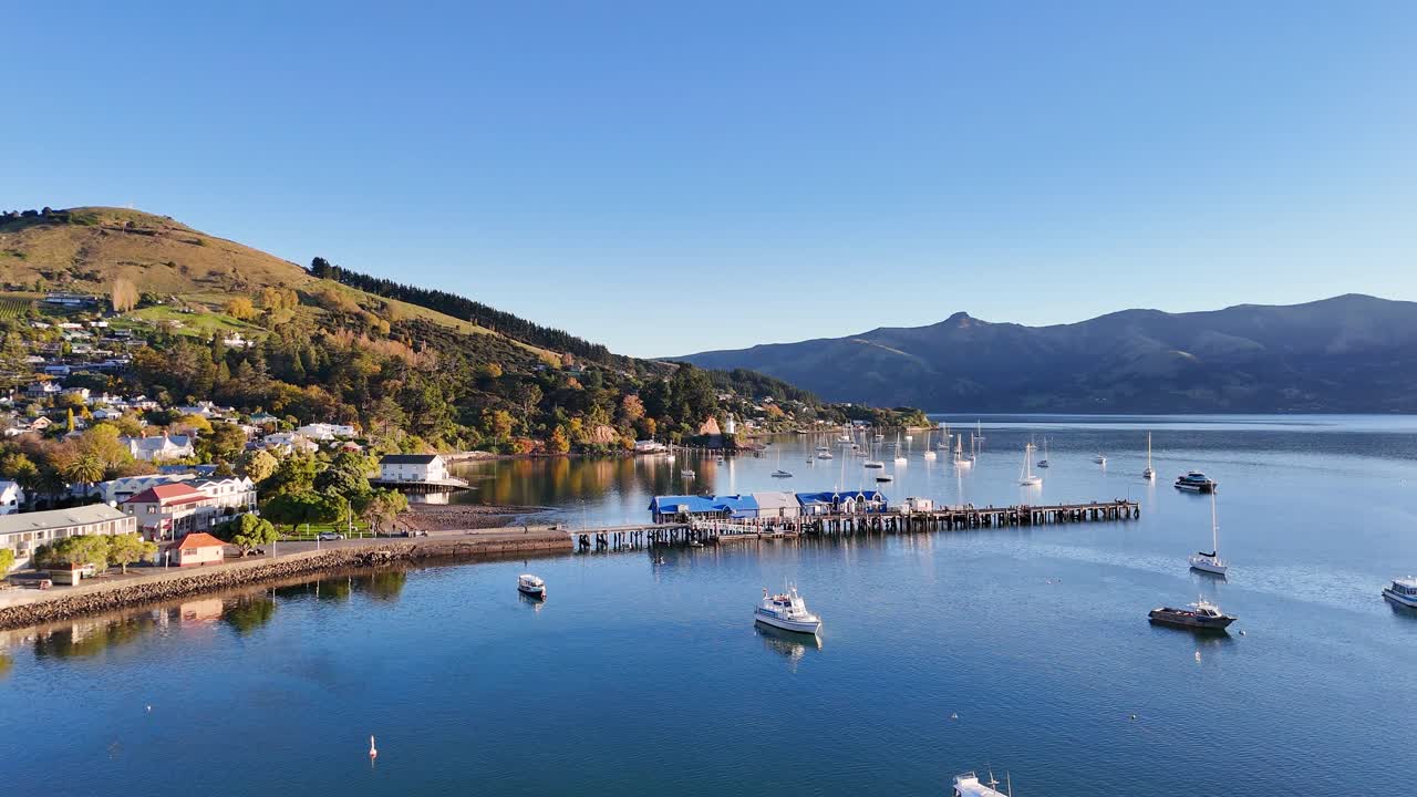 Aerial footage of Akaroa Harbor with boats, hills, and calm waters under sunset lighting