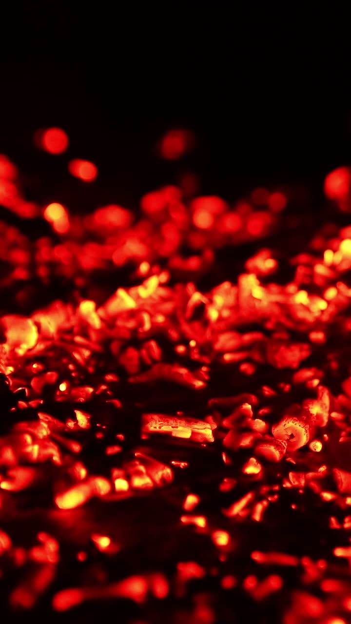 Smoldering red embers scattered on the ground. Smoke goes up and charcoal flashing from the wind. Close up. Vertical video
