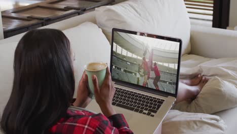 Composite-of-woman-sitting-at-home-holding-coffee-watching-rugby-match-on-laptop