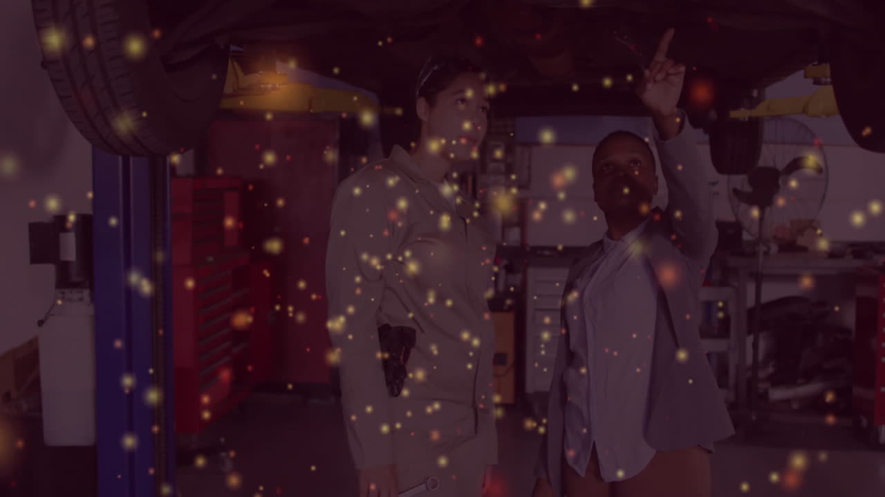 Two women examining lifted vehicle underbody in automotive repair shop, with animated sparks