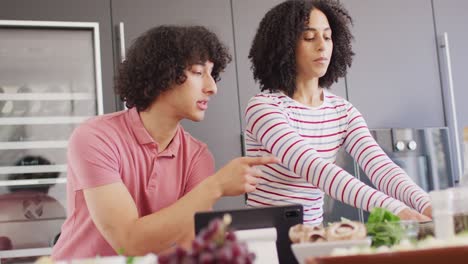 feliz pareja biracial cocinando la cena y usando la tableta en la cocina juntos