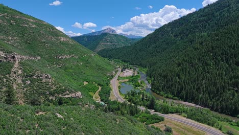 flying along the slate river and a forested valley with a road through the middle near the, colorado, usa