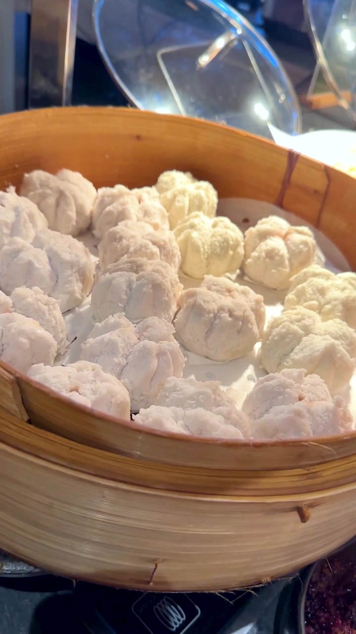 Một bàn tay nhấc nắp tre, để lộ những chiếc bánh bao hấp tươi ngon tại quầy buffet nhà hàng