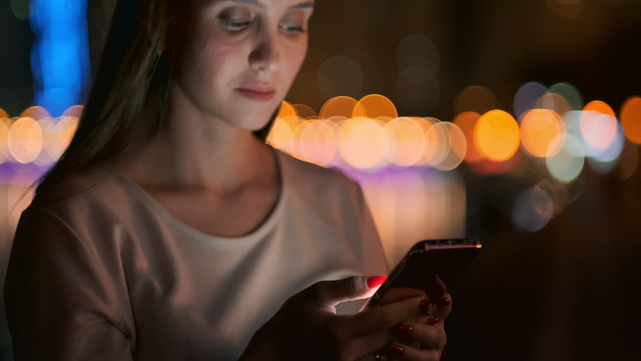 Young woman tourist travels through the night megalopolis and writes text messages on social networks about the journey holds the phone in her hands and looks at the screen of the gadget