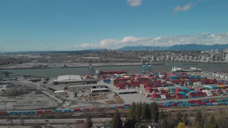 colorful shipping containers stacked high and organized at busy city port harbor dock on edge of fraser river in surrey bc near delta bc in canada aerial wide ascending