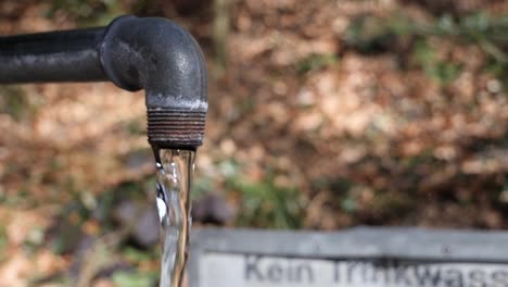 crystal clear water flowing out of a rusty pipe in the woods in switzerland