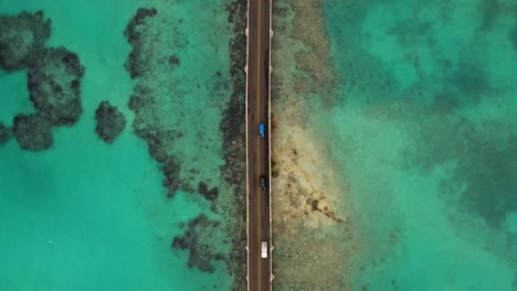 birds eye view following car bridge over turquoise water on tropical island