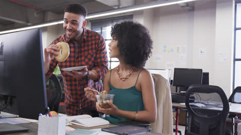 Happy-diverse-male-and-female-colleagues-eating-and-talking-at-desk-in-office,-slow-motion