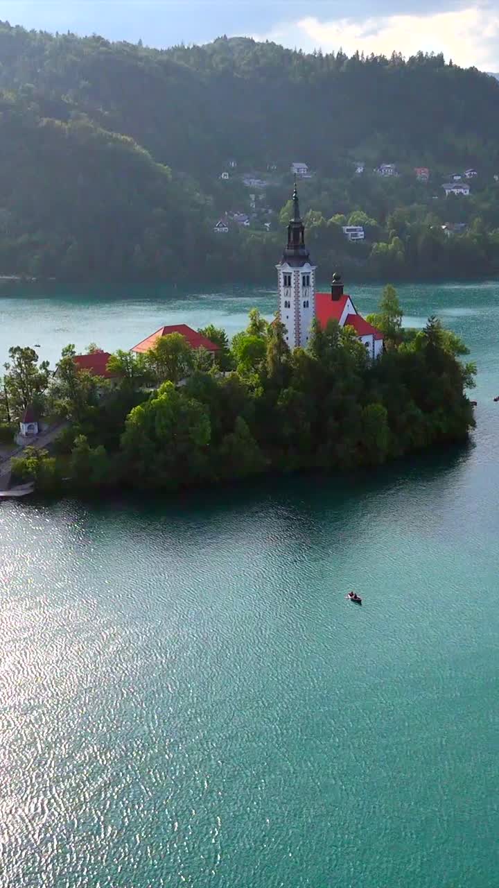 Isola con chiesa sul Lago di Bled che si svela, ripresa aerea cinematografica con tilt verticale verso l'alto, drone che sorvola il lago.