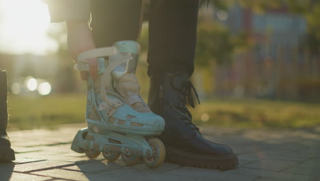 una toma de primer plano de una persona sin rostro de pie en un parque durante un día soleado, con un pie en una patineta azul claro y el otro en una bota negra. el contraste entre los dos tipos de calzado