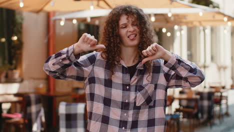 Upset young woman girl showing thumbs down sign disapproval dissatisfied bad work mistake in city