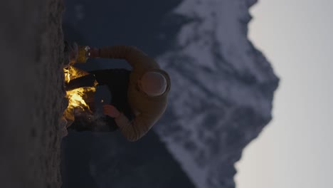 peaceful young man sitting down by campfire, opening beer can