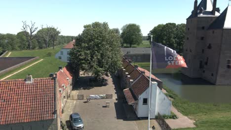 Drone-Volando-Alrededor-De-La-Bandera-Del-Castillo-Loevestein-Revelando-El-Monumento-De-La-Unesco-En-El-Fondo-En-Un-Brillante-Día-Soleado-En-Los-Países-Bajos