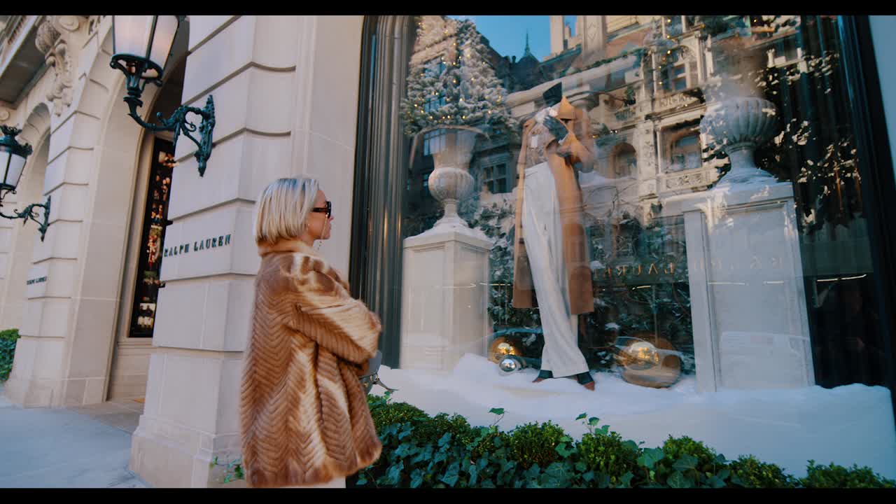 New York, USA, 9 ottobre 2025: Donna che osserva una vetrina natalizia su Madison Avenue, New York. Ampia inquadratura di una donna in pelliccia in piedi fuori da una boutique di lusso con decorazioni natalizie.