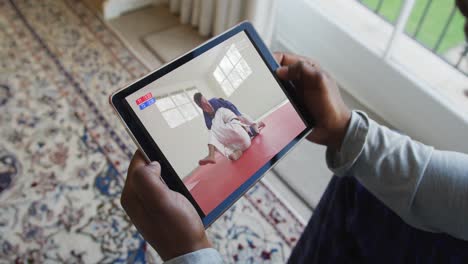 Composite-of-man-sitting-at-home,-watching-judo-match-on-tablet