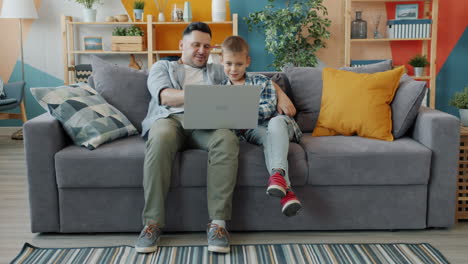 father and son using laptop on couch