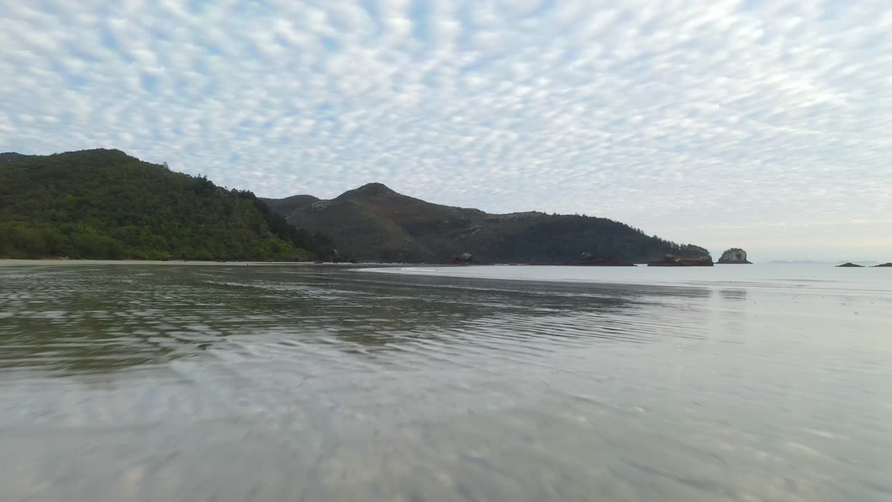 해안만의 아름다운 빈 해변, 석양의 모래 위로 낮은 공중 비행