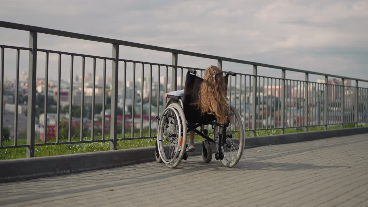 una niña se sienta en silla de ruedas mirando el panorama de la ciudad