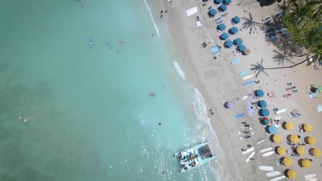 un avión no tripulado captura la escena idílica de una playa blanca, paraguas vibrantes, y la gente nadando en el mar claro y acogedor