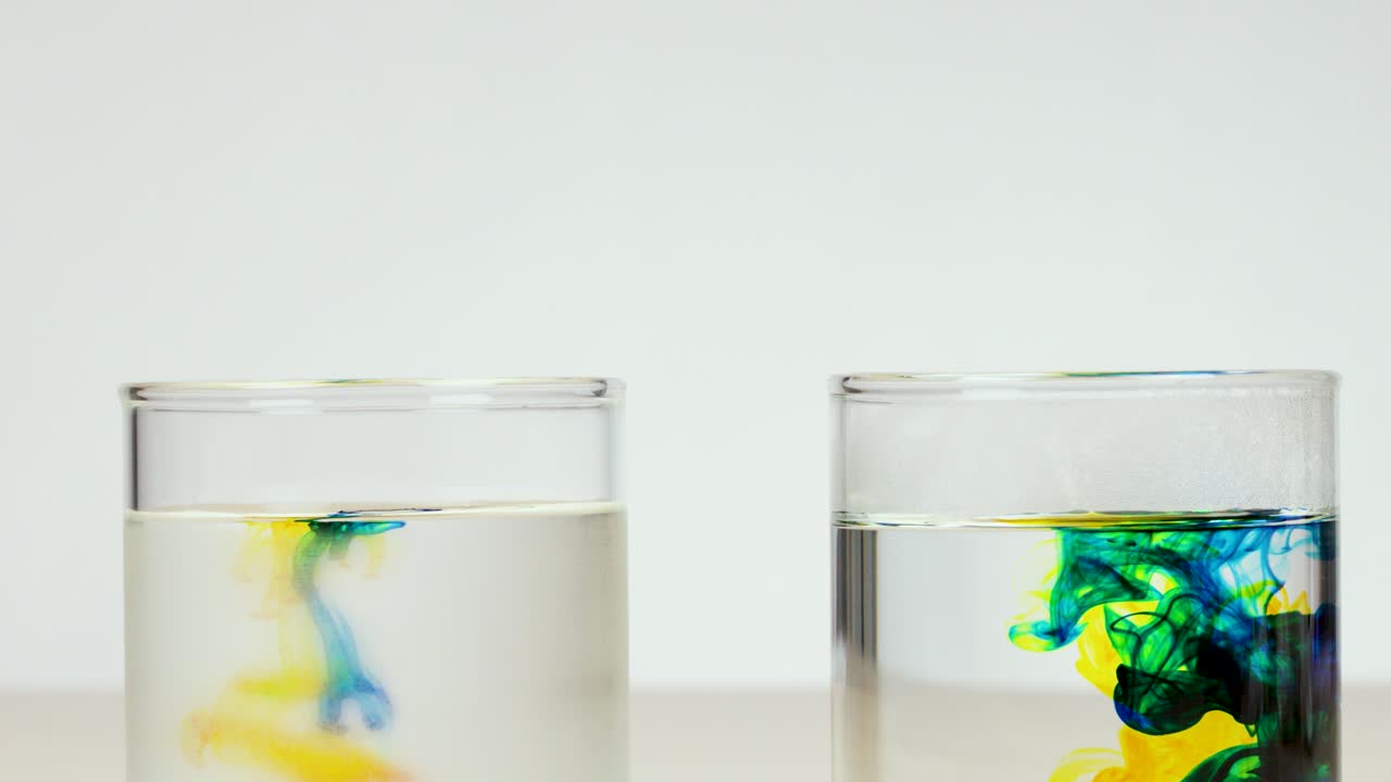 Food coloring disperses in clear water, captured in bright lighting with a static camera
