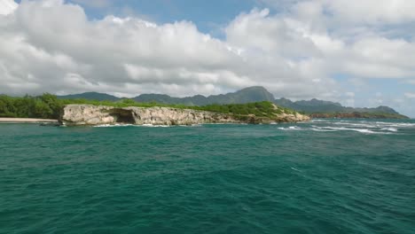 Approach-to-cliff-on-Hawaiian-coastline-next-to-turquoise-blue-sea-with-people-hiking-on-top-of-it